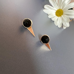 May include: A pair of gold earrings with black gemstone accents. The earrings have a triangular shape with a pointed tip.