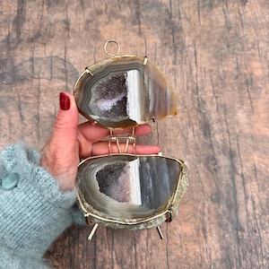May include: A gold metal stand with two agate slices. The agate slices are brown, gray, and white with a crystal-like interior.