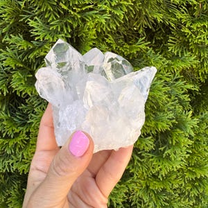 May include: A cluster of clear quartz crystals with multiple points. The crystals are transparent and reflect light, showcasing their natural formations. The background is a vibrant green, providing a contrast to the crystal's clarity. This is a natural mineral specimen.