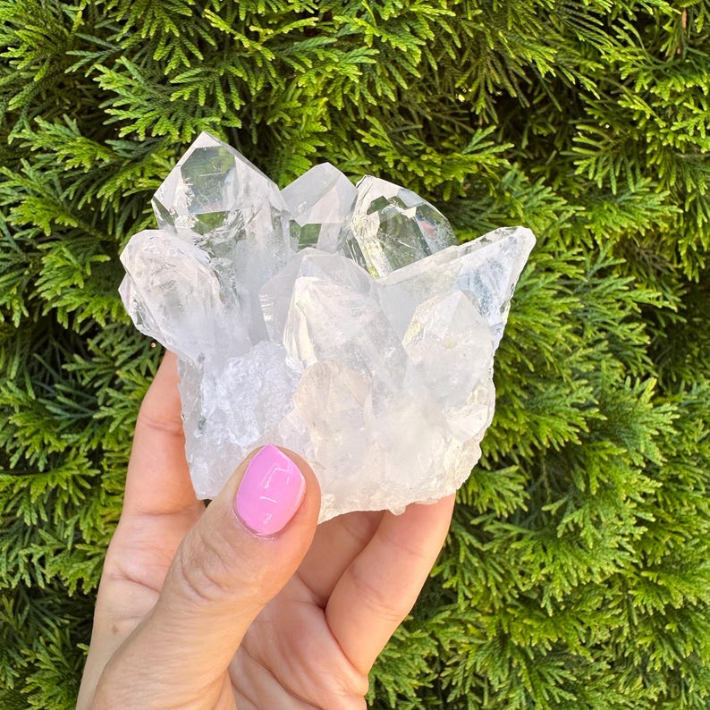 May include: A cluster of clear quartz crystals with multiple points. The crystals are transparent and reflect light, showcasing their natural formations. The background is a vibrant green, providing a contrast to the crystal's clarity. This is a natural mineral specimen.