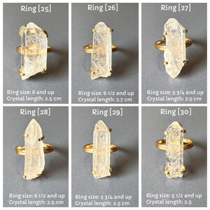 May include: Six gold rings, each with a clear, elongated crystal. The rings are displayed on a grey surface. The crystal lengths vary from 2.5 cm to 2.7 cm. Ring sizes are 6 and up, 6 1/2 and up, and 5 3/4 and up. The image includes text indicating ring size and crystal length.