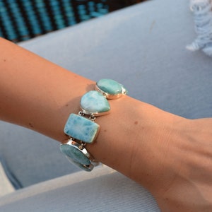 May include: A silver bracelet with blue and green gemstone charms. The bracelet is on a person's wrist.