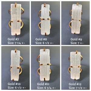 May include: Six gold-toned rings featuring rectangular, translucent white selenite crystals held by metal prongs. Each ring is labelled with a number and a size in inches, ranging from 6 1/2 to 7 1/2, indicating specific ring sizes for each individual piece.