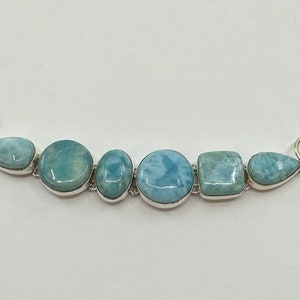 May include: A silver bracelet with a toggle clasp features a row of six blue and white gemstone beads. The beads are various shapes, including round, oval, and square.