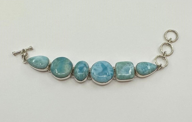 May include: A silver bracelet with a toggle clasp features a row of six blue and white gemstone beads. The beads are various shapes, including round, oval, and square.