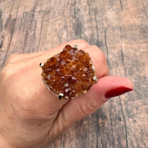 May include: A gold ring with a large, brown, crystal cluster set in the center. The crystal cluster is made up of many small, faceted crystals.