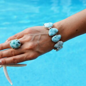 May include: A hand wearing a ring with a large blue and green gemstone and a bracelet with multiple blue and white gemstones. A white starfish is in the hand.