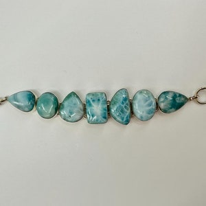 May include: A silver bracelet with a toggle clasp features seven blue and white gemstone beads. The beads are irregularly shaped and have a cloudy, marbled appearance.