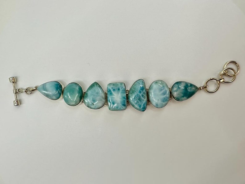 May include: A silver bracelet with a toggle clasp features seven blue and white gemstone beads. The beads are irregularly shaped and have a cloudy, marbled appearance.