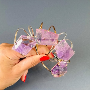 May include: A collection of four bracelets featuring raw, translucent purple amethyst stones set on thin, curved metallic bands. The stones have irregular, faceted edges and are securely attached to the gold and silver-toned wire frames.