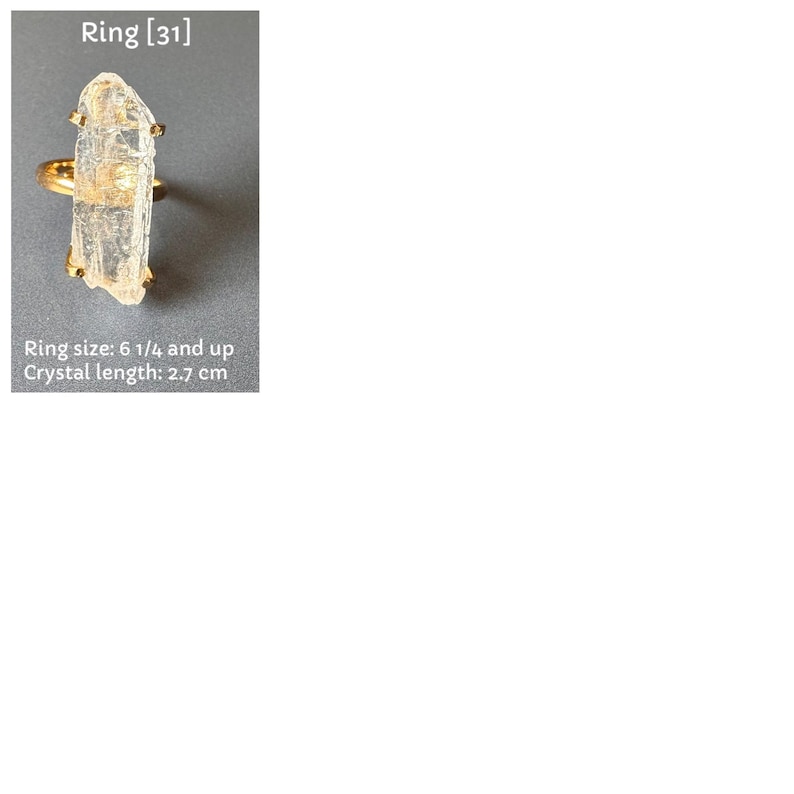 May include: A gold ring with a clear, rectangular crystal. The crystal measures approximately 2.7 cm in length. Ring size is 6 1/4 and up. The image includes the text "Ring [31]" and "Ring size: 6 1/4 and up Crystal length: 2.7 cm".