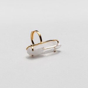 May include: A gold ring with a clear quartz crystal. The quartz is rectangular and set horizontally in a gold frame. The ring band is a simple, curved design.