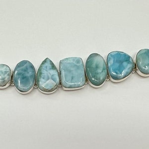 May include: A silver bracelet with a chain clasp and seven light blue and white gemstone beads. The beads are all different shapes and sizes.