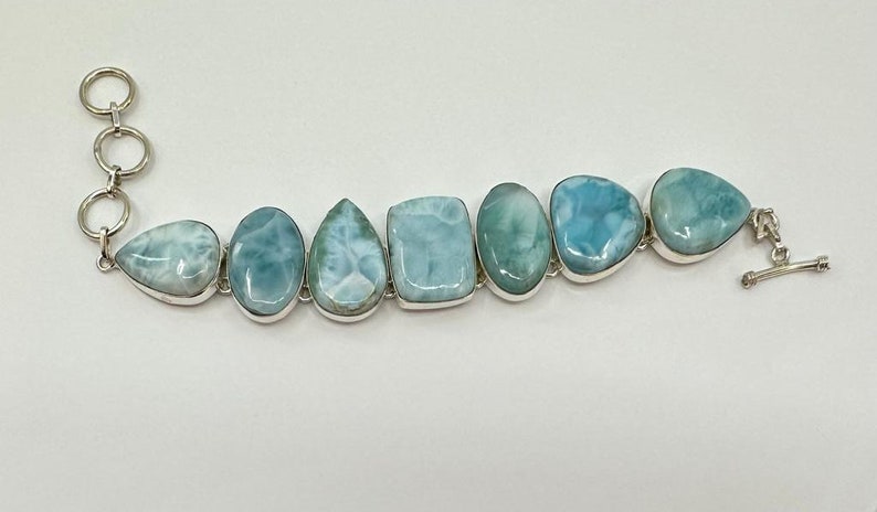 May include: A silver bracelet with a chain clasp and seven light blue and white gemstone beads. The beads are all different shapes and sizes.