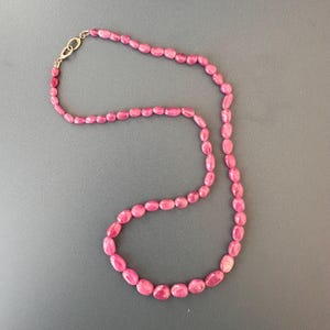 May include: A long pink gemstone necklace with oval-shaped beads.