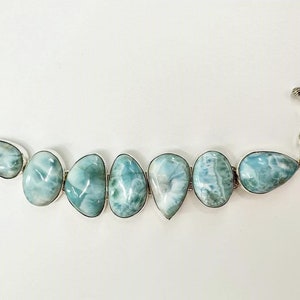 May include: A silver bracelet with a toggle clasp features a row of seven teardrop-shaped blue and white gemstone beads.