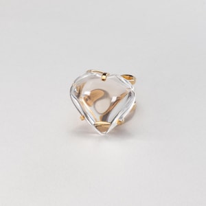 May include: A clear, heart-shaped ring with a gold band and accents. The ring's heart is faceted, catching light and creating a sparkling effect. The gold band adds a touch of elegance to this unique piece of jewelry.