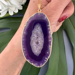 May include: A gold chain necklace with a large purple agate pendant. The pendant is oval shaped and has a gold rim.
