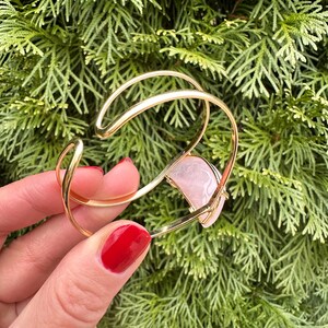 May include: A gold bangle bracelet with a pink rose quartz stone set into the design.