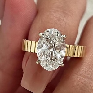 以下が含まれることがあります： 大きな楕円形のダイヤモンドが付いた金の指輪。指輪はテクスチャ加工されたバンドです。
