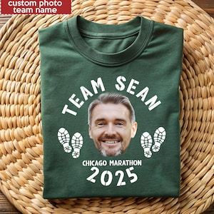 以下が含まれることがあります： 「TEAM SEAN」の文字と男性の写真がプリントされた濃い緑色のTシャツ。「CHICAGO MARATHON 2025」の文字と白い足跡が2組、写真の下にあります。左上には「custom photo team name」の文字があります。
