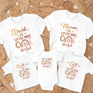 May include: Set of five white t-shirts with a rainbow and the text "Little Miss One Derful" in pink and gold. The shirts have different titles: "Daddy", "Mommy", "Brother", "Sister", and "Little Miss One Derful".