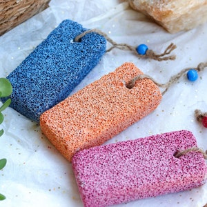 Puede incluir: Tres piedras pómez con cuerda y cuentas para colgar. Las piedras son azules, naranjas y rosas.