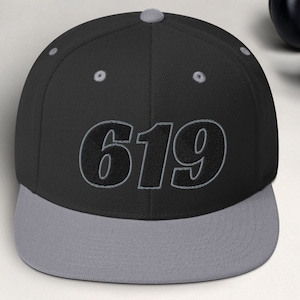 Puede incluir: Una gorra de béisbol negra y gris con el número "619" bordado en negro en la parte delantera.