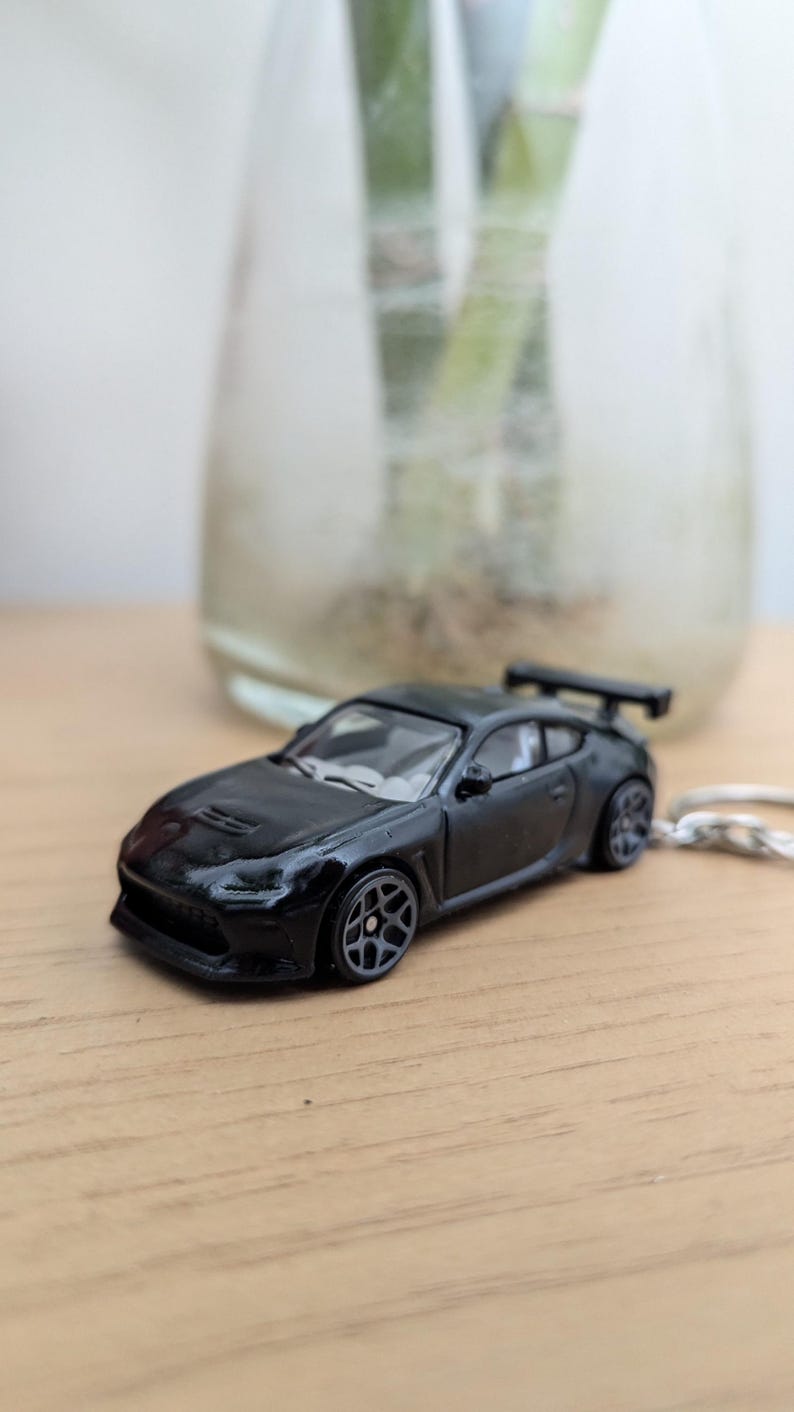 May include: A black toy car with a rear spoiler and gray wheels. The car is sitting on a wooden surface.