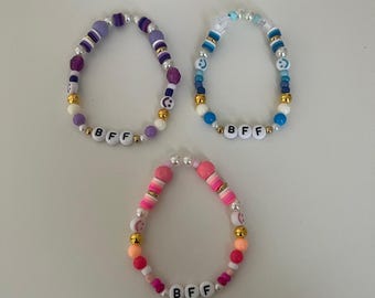 May include: Three beaded bracelets with the word "BFF" spelled out in white letters. The bracelets are made with colorful beads, including purple, blue, pink, white, and gold.
