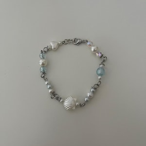 May include: A silver bracelet with white and blue beads, a silver heart charm, and a silver seashell charm.