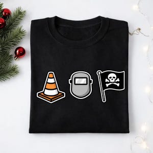 May include: Black sweatshirt featuring three graphic designs: an orange and white traffic cone, a gray welding mask, and a black pirate flag with a skull and crossbones. The sweatshirt is made of a soft material.