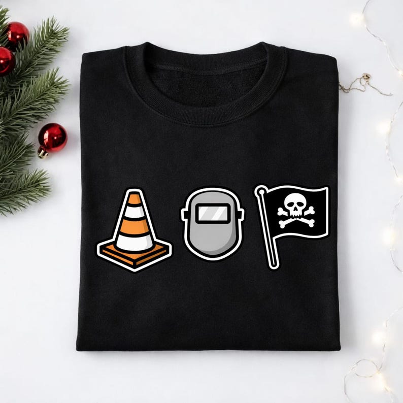 May include: Black sweatshirt featuring three graphic designs: an orange and white traffic cone, a gray welding mask, and a black pirate flag with a skull and crossbones. The sweatshirt is made of a soft material.