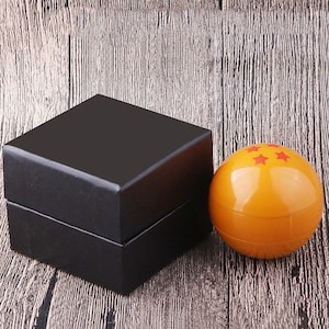 May include: A black box with a shiny orange sphere with red stars on it. The sphere is a Dragon Ball.
