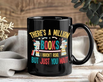 May include: Black ceramic mug with a large handle. The mug features the text "THERE'S A MILLION BOOKS I HAVEN'T READ, BUT JUST YOU WAIT" in colorful letters, with stacks of books on either side of the text.