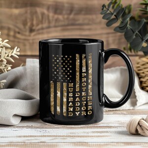 May include: Black ceramic mug featuring a distressed American flag design in shades of brown and gold. The words "PROTECTOR, HUSBAND, DAD" are vertically printed on the right side of the mug. A perfect gift for a loved one.