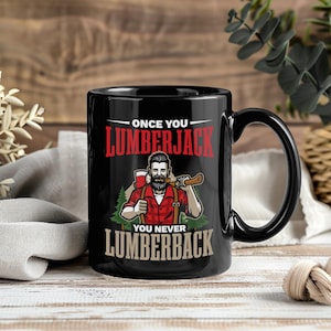 May include: Black ceramic mug with a handle featuring a lumberjack graphic. The design includes a bearded man in a red plaid shirt holding an axe and the text "ONCE YOU LUMBERJACK YOU NEVER LUMBERBACK" in red and beige.