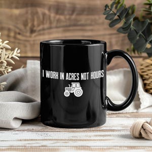 May include: Black ceramic coffee mug with a white tractor graphic and the text "I WORK IN ACRES NOT HOURS". The mug has a large handle and is suitable for hot or cold beverages. Perfect for farmers and agricultural workers.