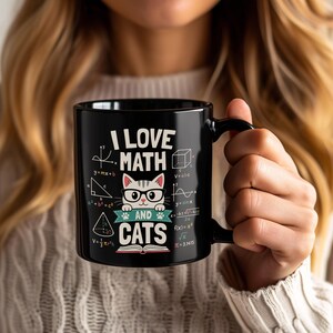 Puede incluir: Una taza de cerámica negra con el gráfico de un gato blanco con gafas negras, situado sobre un libro abierto. El texto dice I LOVE MATH AND CATS, rodeado de varias fórmulas matemáticas, formas geométricas y pequeñas huellas de patas.