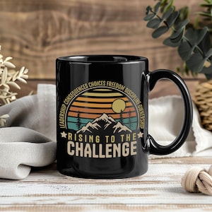 May include: Black ceramic mug with a wraparound design featuring a mountain scene with a sunset and the text "RISING TO THE CHALLENGE." The mug also includes the words "LEADERSHIP CONSEQUENCES CHOICES FREEDOM DISCIPLINE OWNERSHIP."