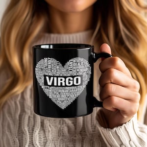 May include: Black ceramic mug featuring the word "VIRGO" in white, surrounded by a heart-shaped design composed of words like "loyal," "creative," and "intellectual." The mug has a black handle and is held by a person.