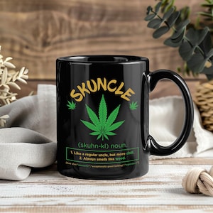 May include: Black ceramic mug with the word "SKUNCLE" in gold lettering, featuring a green cannabis leaf. The mug includes definitions: "Like a regular uncle, but more chill. Always smells like weed."