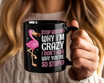 May include: Black ceramic mug featuring a pink flamingo illustration and the text "STOP ASKING WHY I'M CRAZY I DON'T ASK WHY YOU'RE SO STUPID". The mug has a black handle and a white interior.