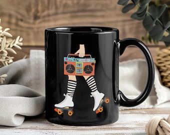 May include: Black ceramic mug featuring a retro illustration. The design depicts a person's legs in roller skates and striped socks, holding a boombox. The boombox is orange and teal. The mug has a black handle and a black interior.