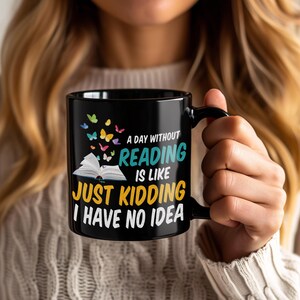 May include: Black ceramic mug with the text "A day without reading is like just kidding I have no idea." The mug features a design of colorful butterflies and an open book. A perfect gift for book lovers.