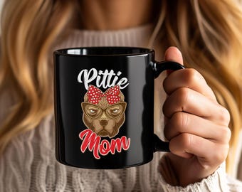 May include: Black ceramic mug featuring a brown pit bull wearing glasses and a red bow. The mug has the words "Pittie Mom" in white and red script.
