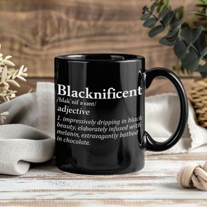 Może przedstawiać: Czarny ceramiczny kubek z napisem "Blacknificent" w białym tekście. Kubek ma definicję pod słowem, opisującą go jako "imponująco ociekający czarnym pięknem, bogato nasycony melaniną, ekstrawagancko skąpany w czekoladzie."