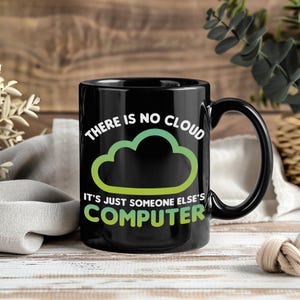 May include: Black ceramic mug featuring a cloud graphic in white and green, with the text "THERE IS NO CLOUD IT'S JUST SOMEONE ELSE'S COMPUTER". The mug has a large handle and is suitable for hot or cold drinks.
