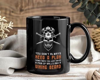 May include: Black ceramic mug with a handle featuring a skull wearing a crown and crossed swords. The mug has the text "YOU DON'T ALWAYS NEED A PLAN SOMETIMES YOU JUST NEED A PAIR OF BALLS AND A VIKING BEARD."