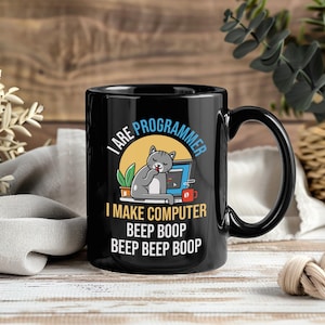 Pode incluir: Caneca de cerâmica preta com um design humorístico. A caneca apresenta o texto "I ARE PROGRAMMER" e "I MAKE COMPUTER BEEP BOOP BEEP BEEP BOOP" com um gato de desenho animado e um gráfico de computador. A caneca tem uma alça preta.